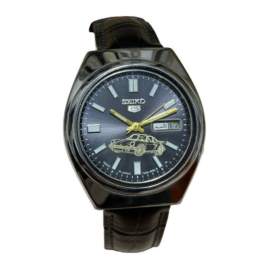 Seiko 5 7009-8360 watch with dark car-motif dial and black strap, on a white background