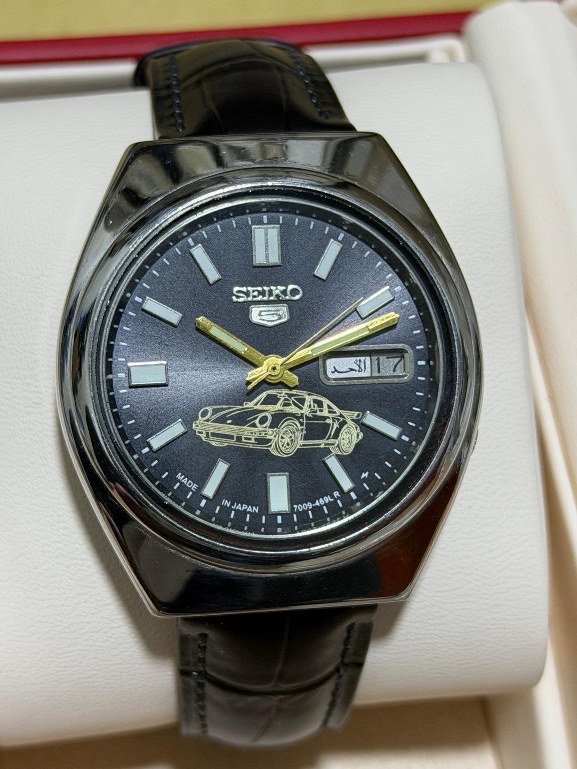 Seiko 5 watch with dark car-motif dial and black strap, front view